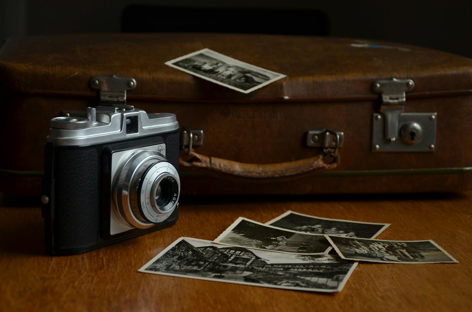A vintage camera alongside old photographs and a leather suitcase on a wooden table.